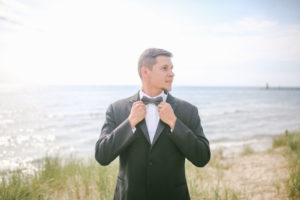 Groom on Lake Michigan beach fixing is tie