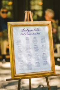 A purple calligraphy seating chart in a gold frame