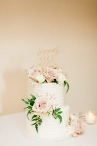 A white cake with dusty pink flowers and a gold Mr. & Mrs. topper