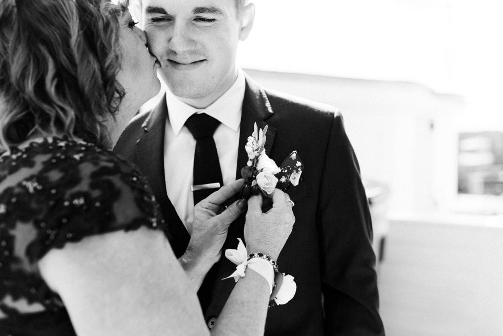 A mother putting a boutonnière on her son before his Loft 310 wedding