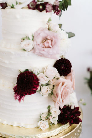 A white wedding cake with blush and burgundy flowers