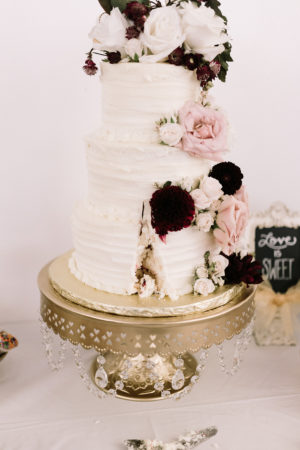 A white wedding cake with blush and burgundy flowers at a Loft 310 wedding