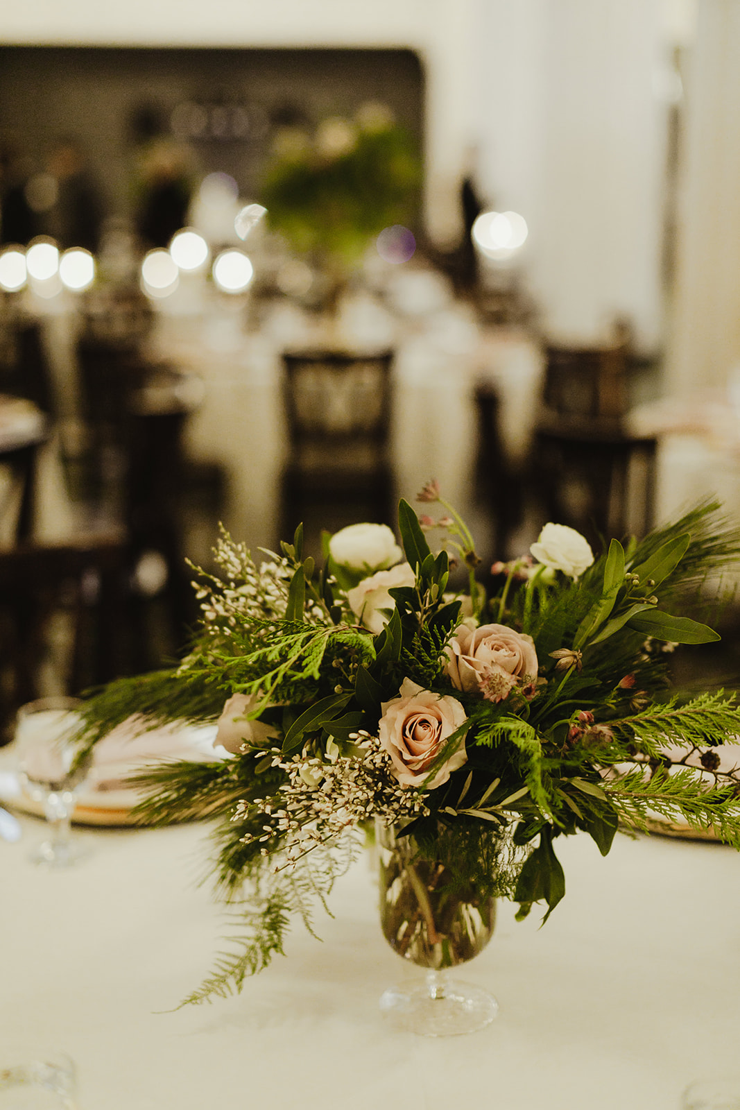 A blush and green floral arrangement on a table at a wedding