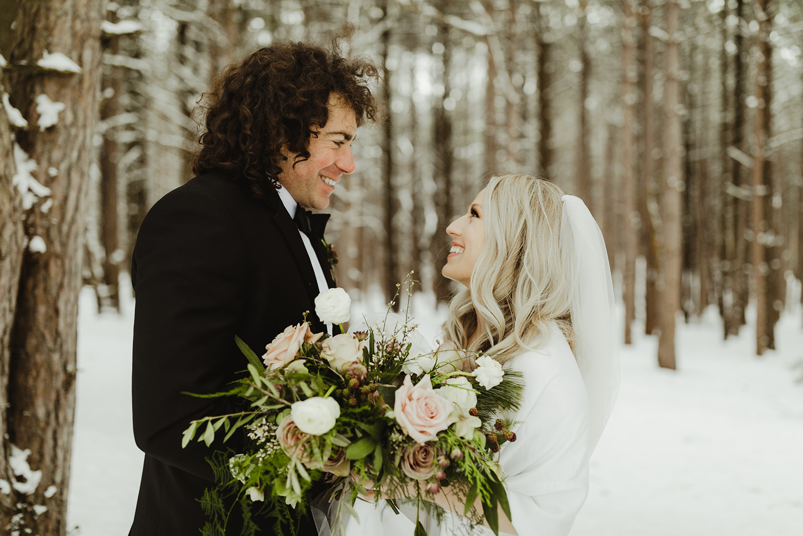 A bride and groom smiling in the snow after their Grand Rapids, Michigan wedding