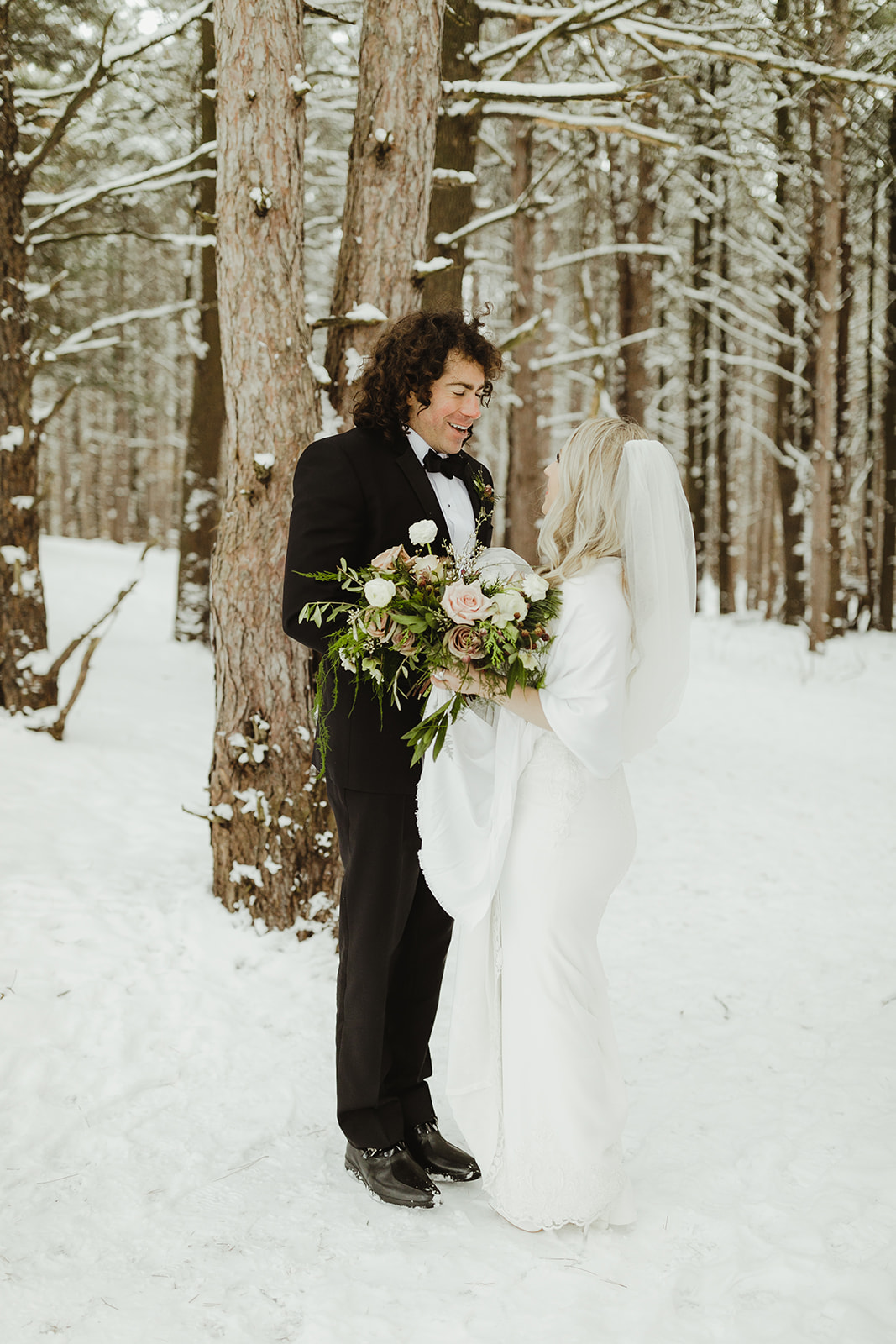 A bride and groom smiling in the snowy woods after their wedding