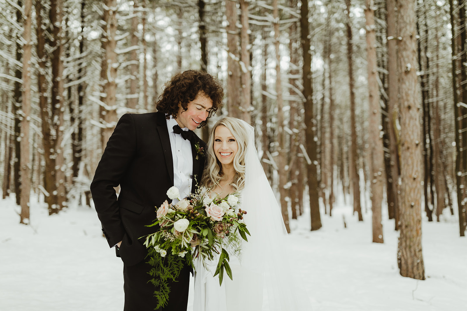 A bride smiling in the snowy woods after her Grand Rapids, Michigan wedding
