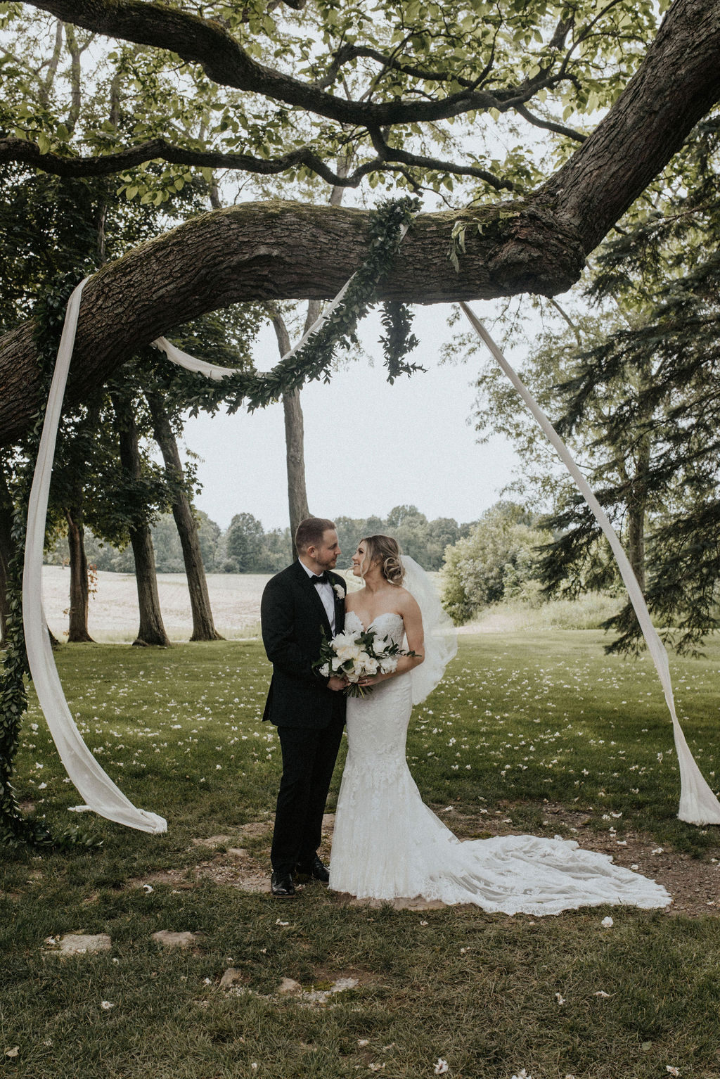 A couple smiling in front of their ceremony tree