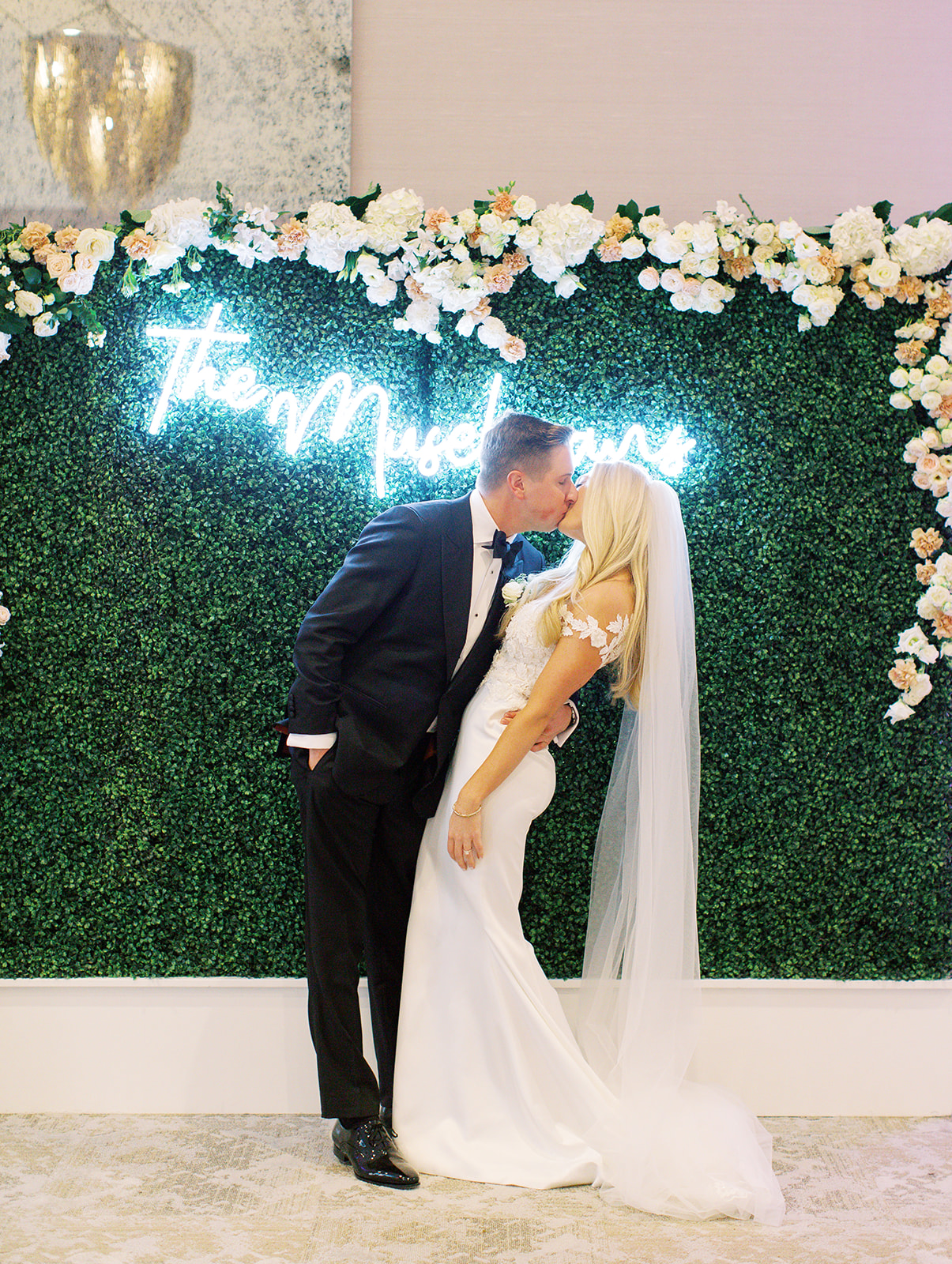 Groom kissing his bride in front of neon sign at Ritz Charles Wedding