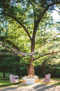 An outdoor cocktail hour with soft seating and hanging lights during a Long Lake Outdoor Center wedding
