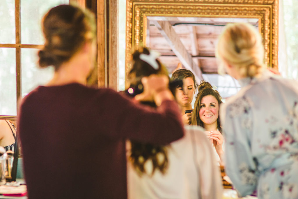 Bride smiling in the mirror while she gets her hair done