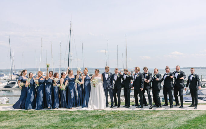 Bride and groom standing with bridesmaids and groomsmen by boat dock.