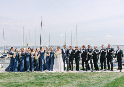 Bride and groom standing with bridesmaids and groomsmen by boat dock.